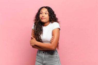 Genç İspanyol kadın omuz silkiyor, kafası karışık ve emin değil, kolları bağlı ve şaşkın görünüyor.