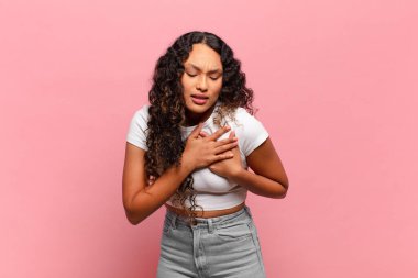 Genç İspanyol kadın üzgün, yaralı ve kalbi kırık görünüyor, iki elini de kalbe yakın tutuyor, ağlıyor ve bunalımda.