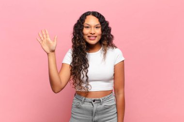 Genç İspanyol kadın mutlu ve neşeyle gülümsüyor, el sallıyor, sizi selamlıyor ya da veda ediyor.