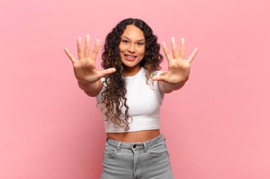 Genç İspanyol kadın gülümsüyor ve arkadaş canlısı görünüyor, onuncu veya onuncu numarayı gösteriyor, eli önde, geriye doğru sayıyor.