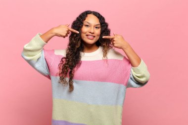 Genç İspanyol kadın kendine güvenerek gülümsüyor. Geniş gülümseme, pozitif, rahat, tatmin olmuş tavır.