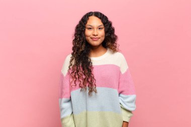 Genç İspanyol kadın pozitif ve kendinden emin gülümsüyor. Tatmin olmuş, arkadaş canlısı ve mutlu görünüyor.