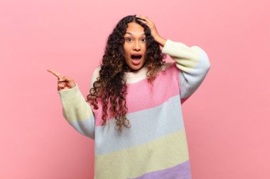 Genç İspanyol kadın gülüyor, mutlu, pozitif ve şaşırmış görünüyor. Yan fotokopi alanını işaret eden harika bir fikrin farkına varıyor.