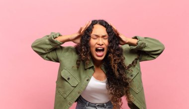 Panik ya da öfke içinde bağıran genç İspanyol kadın, şok olmuş, korkmuş ya da öfkeli, elleri başının yanında.