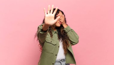 Genç İspanyol kadın yüzünü eliyle kapatıyor ve diğer elini kamerayı durdurmak için öne koyuyor, fotoğraf ya da resimleri reddediyor.