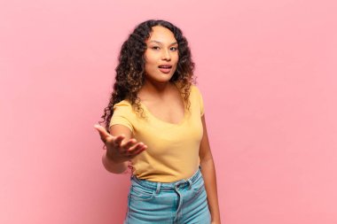 Genç İspanyol kadın gülümsüyor, mutlu, kendinden emin ve arkadaş canlısı görünüyor, bir anlaşmaya varmak için el sıkışmayı teklif ediyor, işbirliği yapıyor.