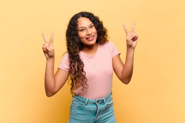 Genç İspanyol kadın gülümsüyor ve mutlu görünüyor, arkadaş canlısı ve tatmin olmuş, zafer ya da barış işareti yapıyor.