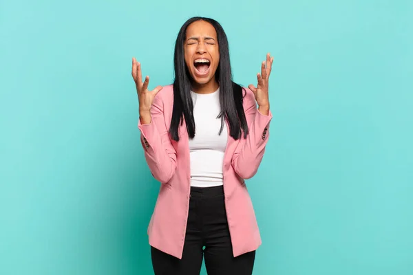 young black woman furiously screaming, feeling stressed and annoyed with hands up in the air saying why me. business concept