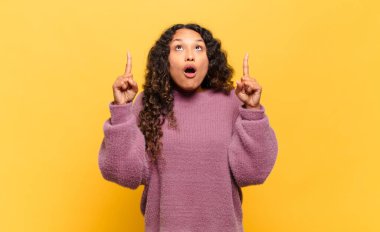 Genç İspanyol kadın şaşırmış, şaşırmış ve ağzı açık görünüyor, iki eliyle boşluğu kopyalamak için yukarı bakıyor.