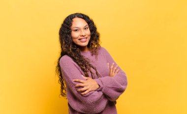 Genç İspanyol kadın kollarını kavuşturup mutlu bir şekilde gülüyor, rahat, pozitif ve tatmin edici bir pozla.