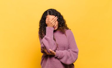 Genç İspanyol kadın stresli, utanmış ya da üzgün görünüyor, baş ağrısı var, yüzünü eliyle kapatıyor.