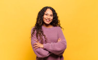 Kollarını kavuşturup gülümseyen mutlu, gururlu ve tatmin olmuş genç bir İspanyol kadın.