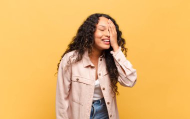 young hispanic woman laughing and slapping forehead like saying doh! 