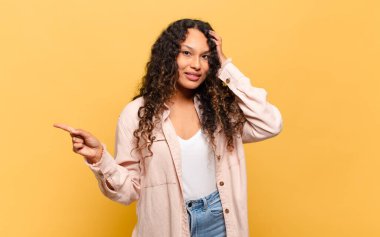 Genç İspanyol kadın gülüyor, mutlu, pozitif ve şaşırmış görünüyor. Yan fotokopi alanını işaret eden harika bir fikrin farkına varıyor.