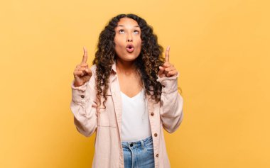 Genç İspanyol kadın şaşkınlık içinde ve ağzı açık. Şok olmuş ve şaşırmış bir bakışla yukarı bakıyor.