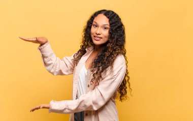 Genç İspanyol bir kadın iki eli yanda bir objeyi tutuyor fotokopi alanında, bir nesneyi gösteriyor, sunuyor ya da reklamını yapıyor.