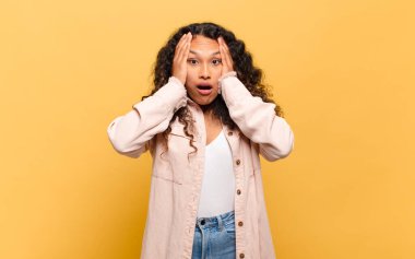 Genç İspanyol kadın hoş olmayan bir şekilde şok olmuş, korkmuş ya da endişeli görünüyor ağzı sonuna kadar açık ve iki kulağını da elleriyle kapatıyor.