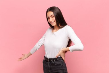 Genç ve güzel bir kadın mutlu ve neşeli hissediyor, gülümsüyor ve seni selamlıyor, dostça bir jestle içeri davet ediyor.