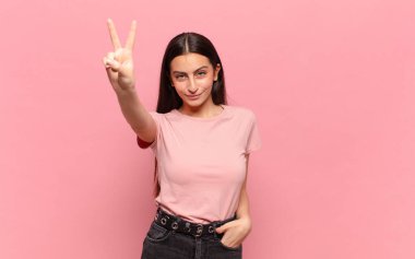 Genç, güzel bir kadın gülümsüyor ve arkadaş canlısı görünüyor. İki ya da iki numarayı gösteriyor. Elleri önde, geri sayıyor.