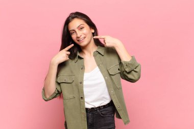 Genç, güzel bir kadın, kendine güvenerek gülümsüyor. Kendi gülüşünü gösteriyor. Olumlu, rahat, tatmin olmuş bir tavır.