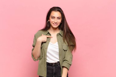 Genç, güzel bir kadın mutlu, gururlu ve şaşırmış görünüyor, neşeli bir şekilde kendini gösteriyor, kendinden emin ve kibirli hissediyor.