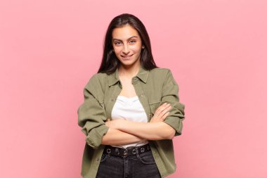 Genç, güzel bir kadın mutlu, gururlu ve tatmin olmuş görünüyor. Kollarını kavuşturup gülümsüyor.