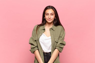 Genç ve güzel bir kadın pozitif ve kendinden emin gülümsüyor. Tatmin olmuş, arkadaş canlısı ve mutlu görünüyor.