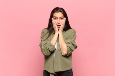 Genç ve güzel bir kadın şok olmuş ve korkmuş hissediyor, ağzı açık ve elleri yanaklarında korkmuş görünüyor.