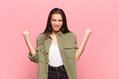 Genç ve güzel bir kadın mutlu, şaşırmış ve gururlanmış hissediyor, bağırıyor ve başarıyı büyük bir gülümsemeyle kutluyor.