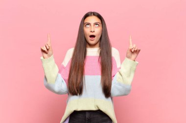 Genç ve güzel bir kadın huşu içinde ve ağzı açık bir şekilde şaşkın ve şaşkın bir bakışla yukarıya bakıyor.