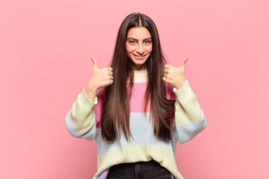 Genç ve güzel bir kadın gülümseyerek mutlu, pozitif, kendinden emin ve başarılı görünüyor.