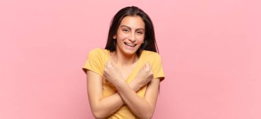 Genç, güzel bir kadın, neşeli bir şekilde gülümsüyor ve kutluyor. Yumruklarını sıkmış, kollarını kavuşturmuş, mutlu ve pozitif hissediyor.