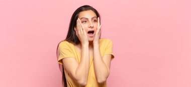 Genç, güzel bir kadın mutlu, heyecanlı ve şaşırmış hissediyor. İki eli de havada bir tarafa bakıyor.