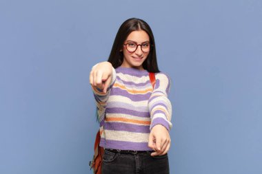 Genç ve güzel bir kadın mutlu ve kendinden emin, kamerayı iki eliyle gösteriyor ve gülüyor, seni seçiyor. öğrenci konsepti