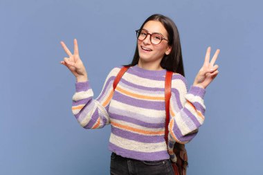 Genç, güzel bir kadın gülümsüyor ve mutlu görünüyor. Dost canlısı ve memnun. İki elinle zafer ya da barış işareti yapıyor. öğrenci konsepti