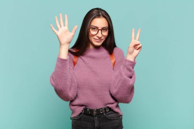 Genç ve güzel bir bayan gülümsüyor ve dost canlısı görünüyor, 7 ya da 7 numarayı gösteriyor, eli önde, geriye doğru sayıyor. öğrenci konsepti