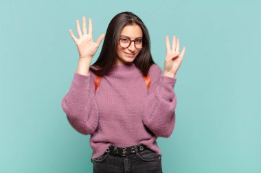 Genç, güzel bir bayan gülümsüyor ve dost canlısı görünüyor. 9 ya da 9 numarayı gösteriyor. Elleri önde, geriye doğru sayıyor. öğrenci konsepti