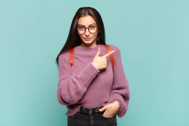 Genç, güzel bir kadın neşeyle gülümsüyor, mutlu hissediyor ve yan ve yukarı doğru işaret ediyor, fotokopi uzayında nesneler gösteriyor. öğrenci konsepti