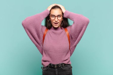 Genç ve güzel bir kadın heyecanlı ve şaşırmış görünüyor, ağzı açık, iki eli de başının üstünde, kendini şanslı hissediyor. öğrenci konsepti