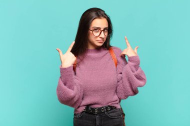 Kötü tavrı olan genç ve güzel bir kadın gururlu ve agresif görünüyor, yukarıyı işaret ediyor ya da elleriyle alay işareti yapıyor. öğrenci konsepti