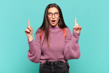 Dehşete kapılmış ve ağzı açık genç bir kadın şaşırmış ve şaşırmış bir bakışla yukarıya bakıyor. öğrenci konsepti