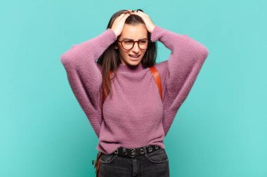 Genç ve güzel bir kadın stresli ve endişeli, depresif ve baş ağrısı ile hayal kırıklığına uğramış hissediyor, iki elini de başa kaldırıyor. öğrenci konsepti