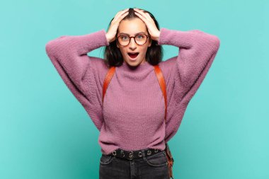 Genç ve güzel bir kadın hoş olmayan bir şekilde şok olmuş, korkmuş ya da endişeli görünüyor ağzı sonuna kadar açık ve iki kulağını da elleriyle kapatıyor. öğrenci konsepti