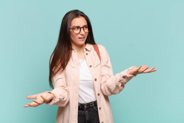 young pretty woman shrugging with a dumb, crazy, confused, puzzled expression, feeling annoyed and clueless. student concept