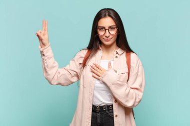 Genç, güzel bir kadın mutlu, kendinden emin ve güvenilir görünüyor, gülümsüyor ve zafer işareti gösteriyor, olumlu bir tavırla. öğrenci konsepti