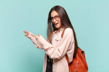 Genç, güzel bir kadın şaşkın ve şaşırmış hissediyor. Kenardaki fotokopi alanını işaret ediyor. Şaşırmış, ağzı açık bir bakışla. öğrenci konsepti