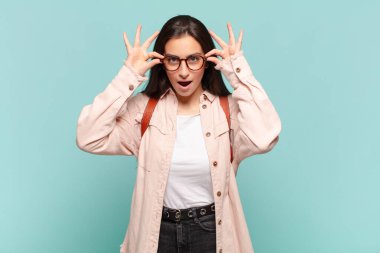 Genç, güzel bir kadın şaşkın, şaşırmış ve şaşırmış hissediyor. Elinde şaşkın ve inanmayan bir bakışla gözlük tutuyor. öğrenci konsepti