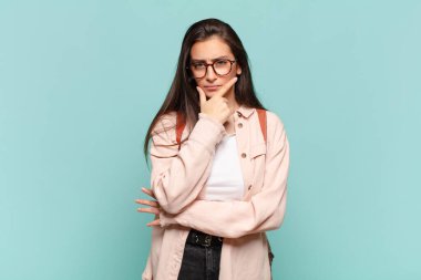 Genç ve güzel bir kadın ciddi, düşünceli ve güvensiz görünüyor, bir kolu çapraz ve elleri çenesinde, seçenekleri değerlendiriyor. öğrenci konsepti