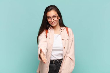 Genç, güzel bir kadın gülümsüyor, mutlu, kendinden emin ve arkadaş canlısı görünüyor, bir anlaşmaya varmak için el sıkışmayı teklif ediyor, işbirliği yapıyor. öğrenci konsepti