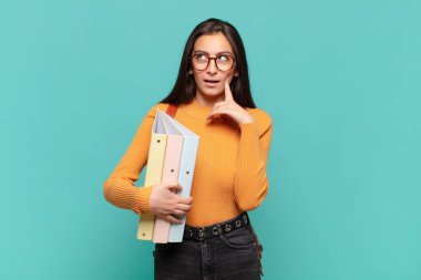 Genç ve güzel bir kadın mutlu bir şekilde gülümsüyor ve hayal kuruyor ya da şüphe ediyor, yan tarafa bakıyor. öğrenci konsepti